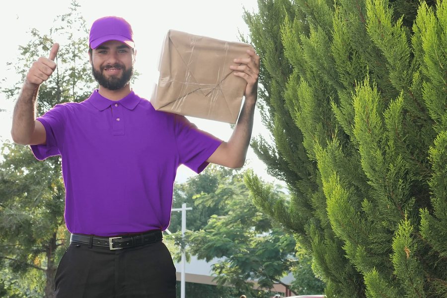 Smiling courier holding a parcel and giving a thumbs-up